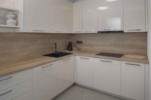 A modern kitchen with white cabinets, a black sink, and a wooden countertop. - Holiday Apartment Apartman Blue (Poreč)
