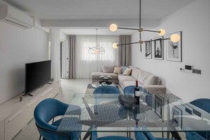 A modern living room with a glass dining table, blue chairs, a sofa, and a flat-screen TV. - Holiday Apartment Apartman Blue (Poreč)