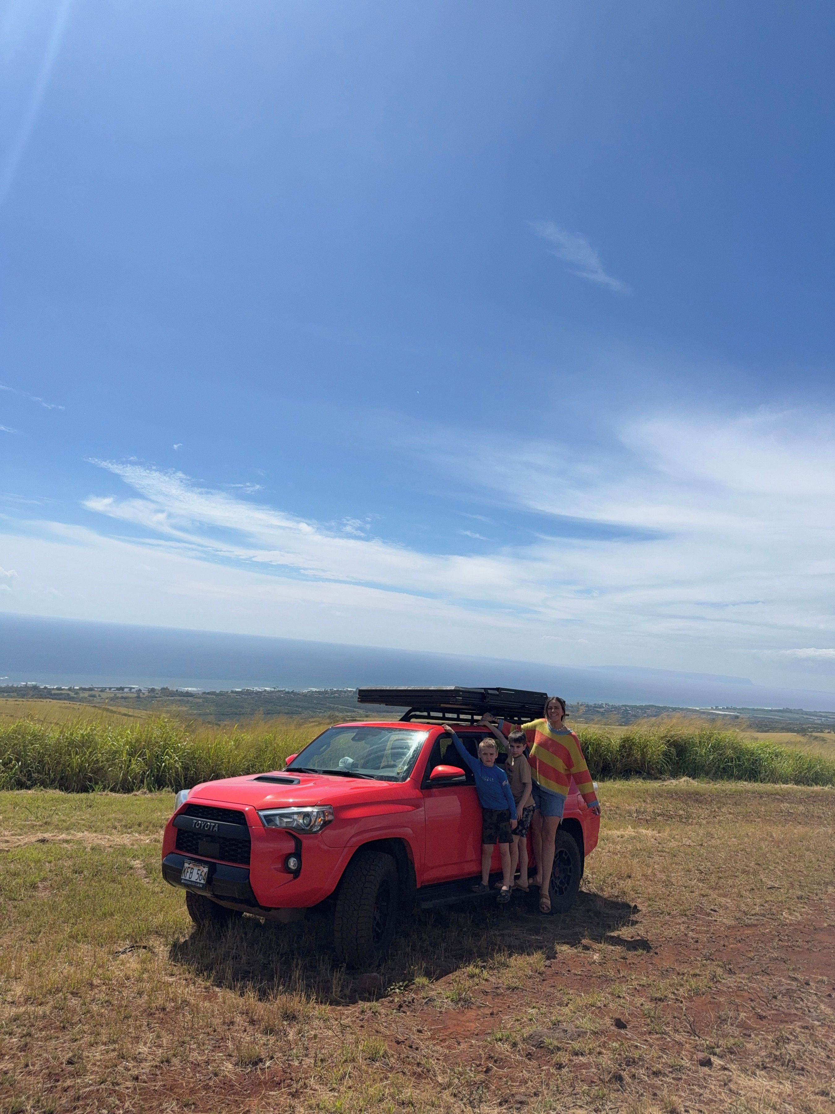 A red off-road vehicle parked on a grassy field with a clear sky and distant landscape.