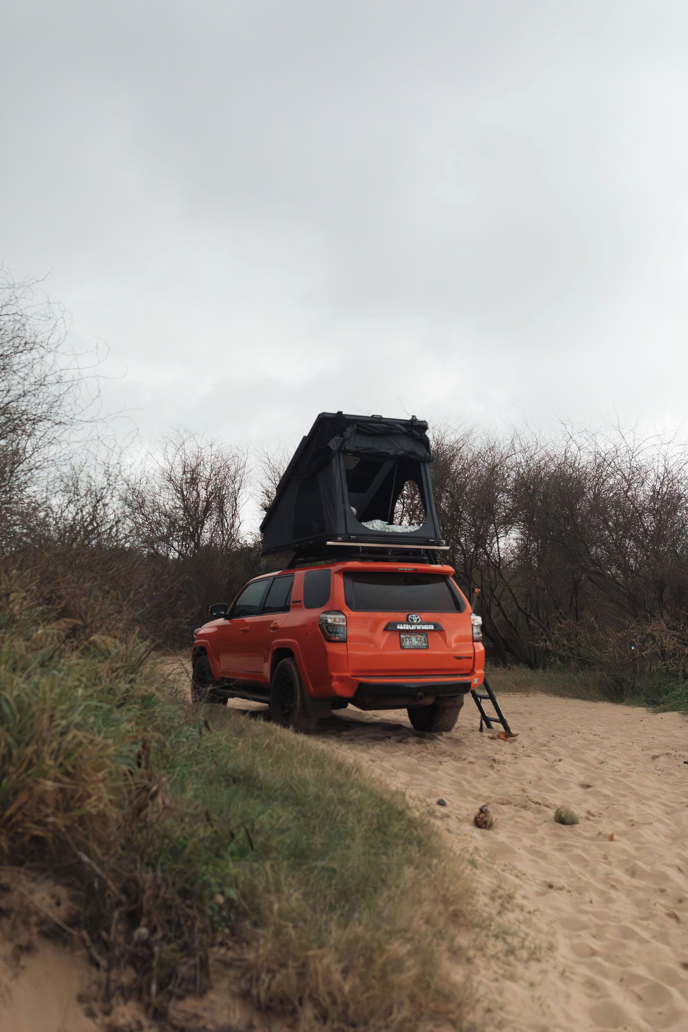 A red SUV parked on a sandy path with a roof tent attached.