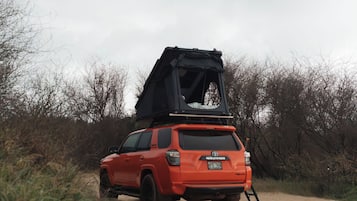 A red SUV parked on a sandy path with a roof tent attached.