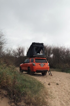 A red SUV parked on a sandy path with a roof tent attached.