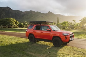 Un SUV rojo estacionado en un césped con montañas al fondo.