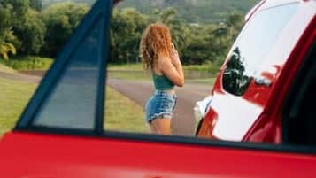 Un auto rojo con un espejo retrovisor que refleja a una persona de pie afuera.