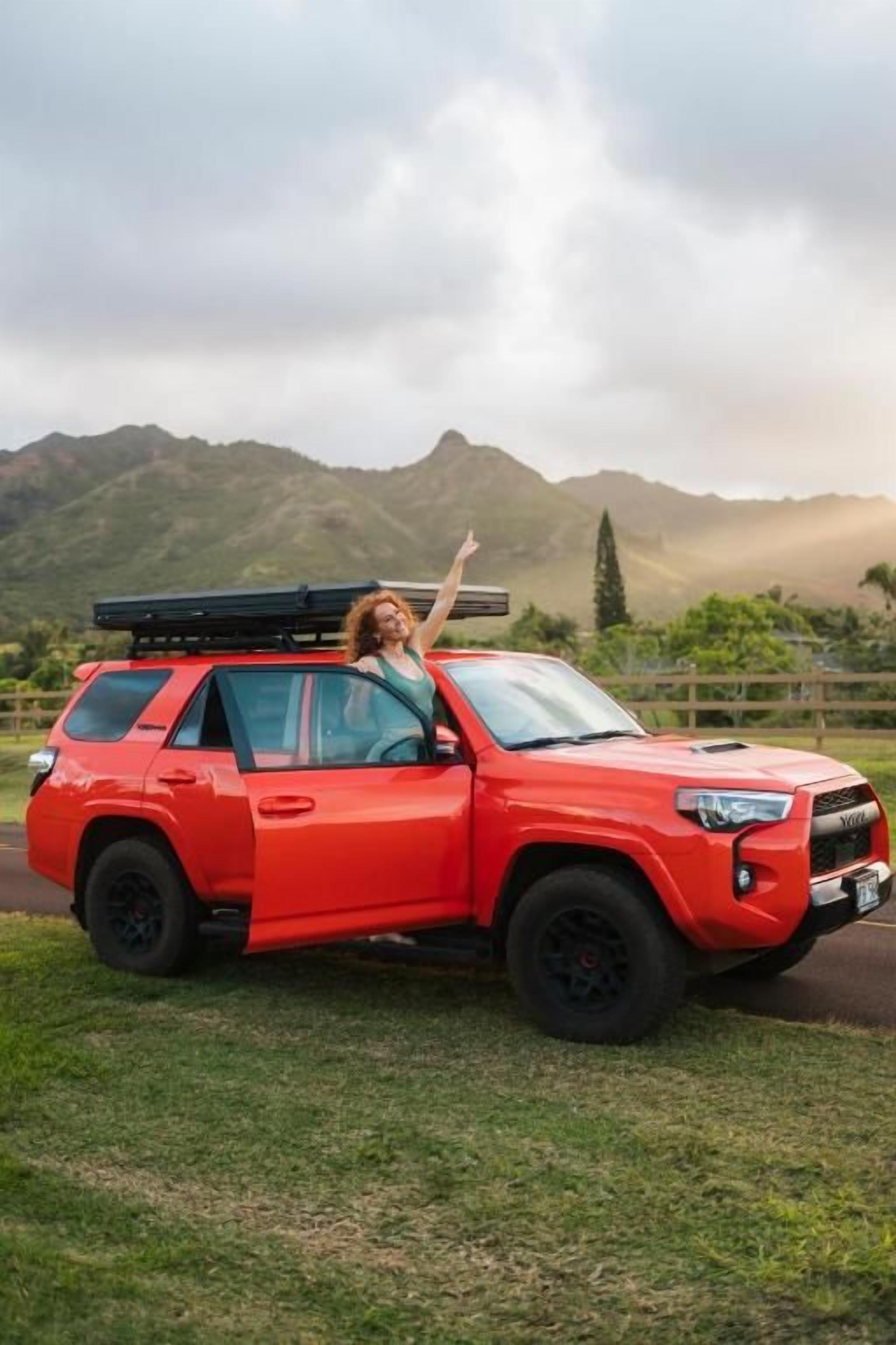 A red SUV parked on a grassy area with a mountainous backdrop.
