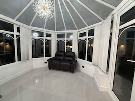 A conservatory with a black leather sofa, large windows, and a chandelier.