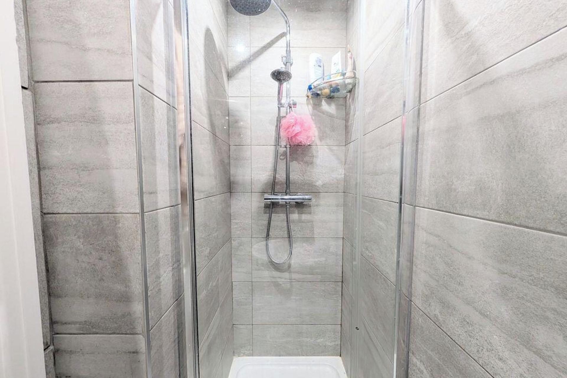 A narrow shower stall with a handheld showerhead and a handheld scrubber.