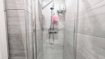 A narrow shower stall with a handheld showerhead and a handheld scrubber.