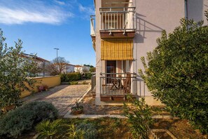 Ein Gebäude mit Balkon, gepflastertem Innenhof und umliegender Bepflanzung.