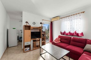 Ein Wohnzimmer mit einem roten Sofa, einer TV-Konsole und einem Essbereich inklusive weißem Kühlschrank.