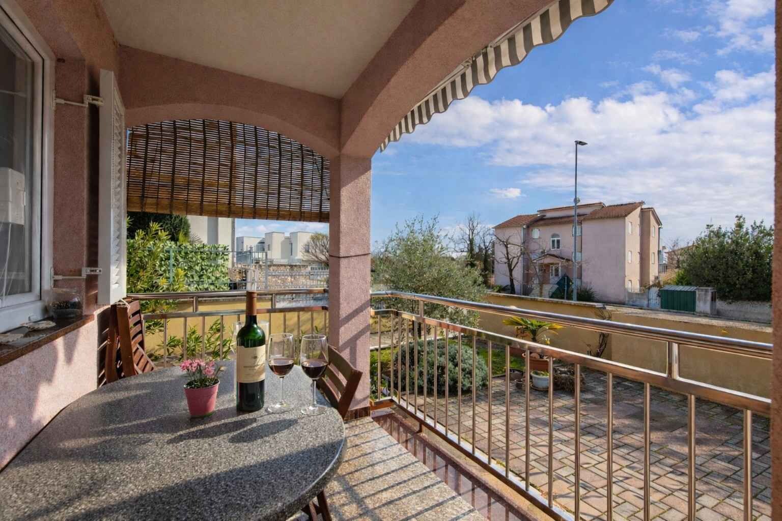 A balcony with a table, chairs, a bottle of wine, and glasses.