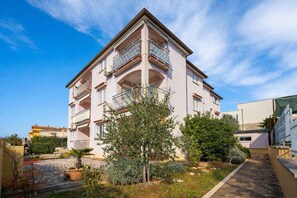 En flervåningsbostadsbyggnad med balkonger, en stenlagd innergård och omgivande grönska.