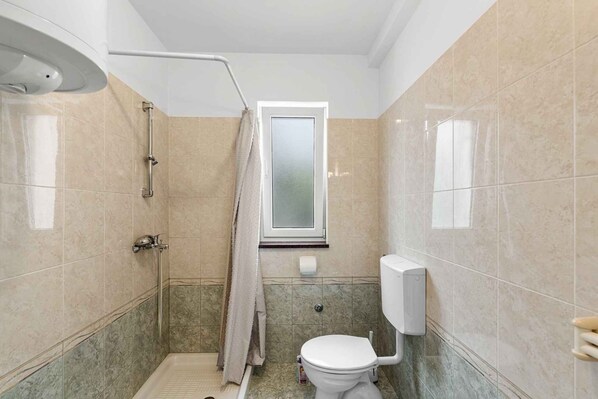 Ein kleines Badezimmer mit Dusche, Toilette und Fenster.