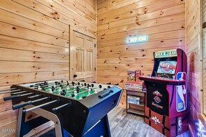 Une pièce avec un baby-foot, une borne d’arcade du jeu NBA JAM et un panneau lumineux au néon.