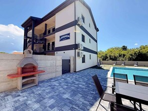 A modern building with a pool, outdoor seating, and a barbecue area. - Holiday apartment with shared use of pool (Polje/Krk)