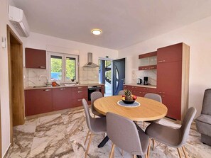 A modern kitchen with a round dining table, grey chairs, and red cabinets. - Holiday apartment with shared use of pool (Polje/Krk)
