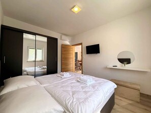 A modern bedroom with a large bed, a wardrobe, a television, and a small round mirror. - Holiday apartment with shared use of pool (Polje/Krk)