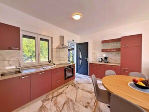 A modern kitchen with red cabinets, a marble countertop, and a dining area with a table and chairs. - Holiday apartment with shared use of pool (Polje/Krk)