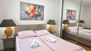 A hotel room with a bed, two bedside lamps, a mirror, and a large abstract painting on the wall. - Holiday Apartment No. 2 Tranquility (Baška)