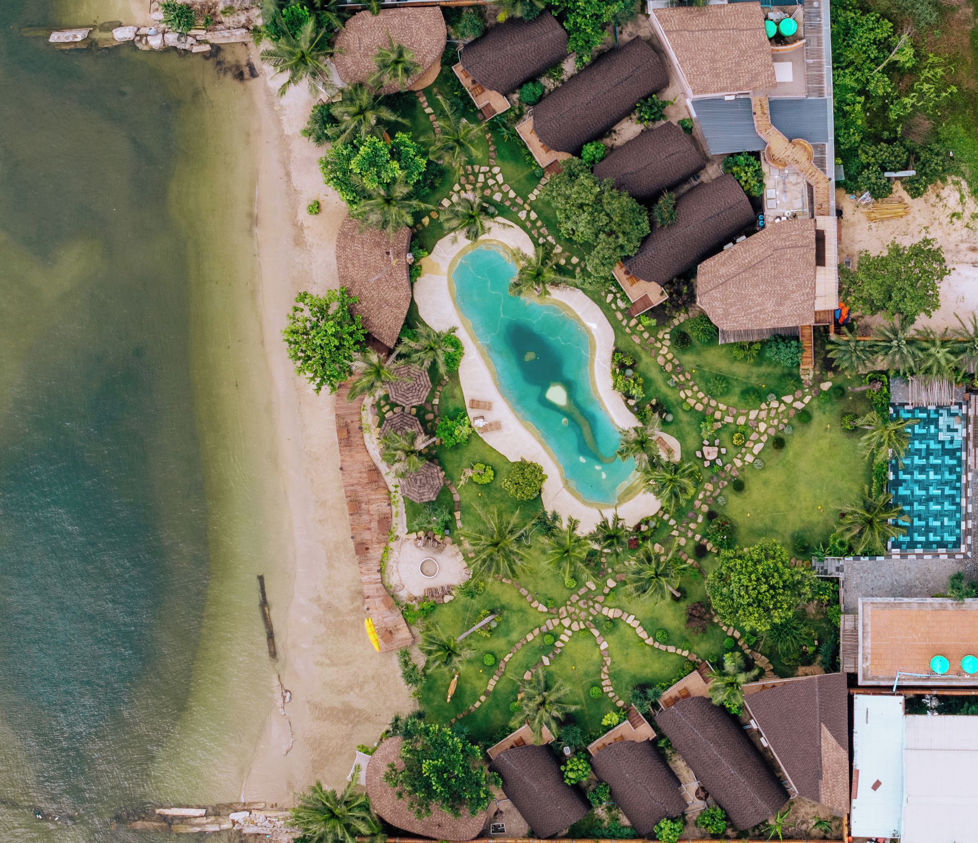 Oversigtsbillede af et resort med swimmingpool, strand og bungalows.