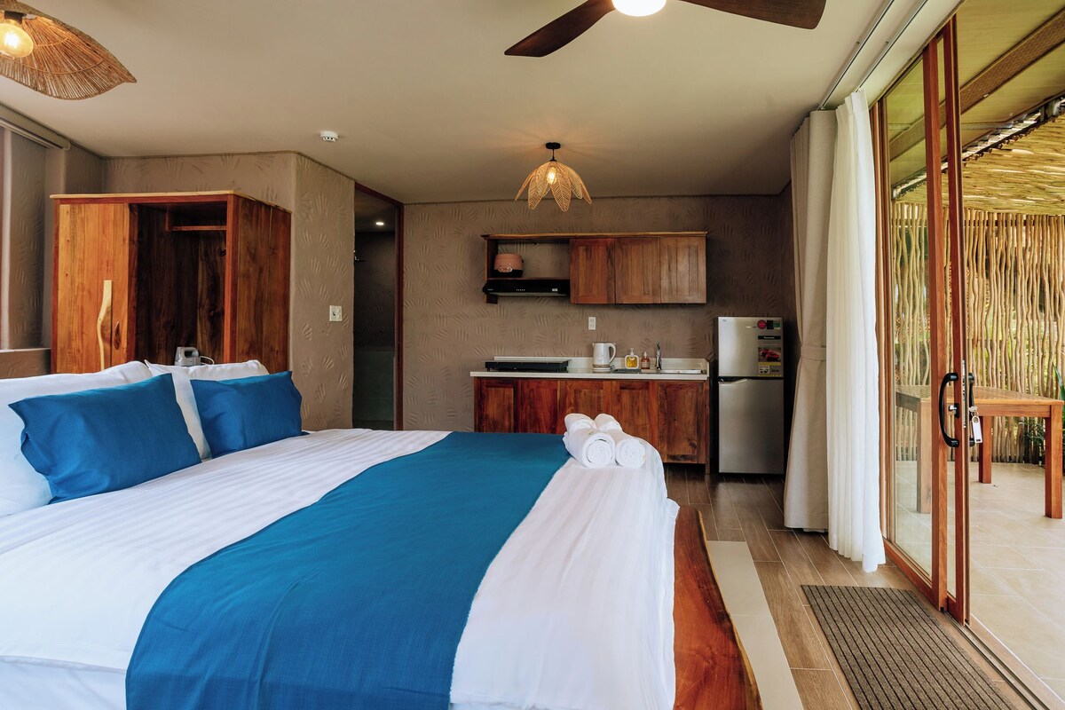 A hotel room with a bed, a kitchenette, and a sliding glass door to the outside.