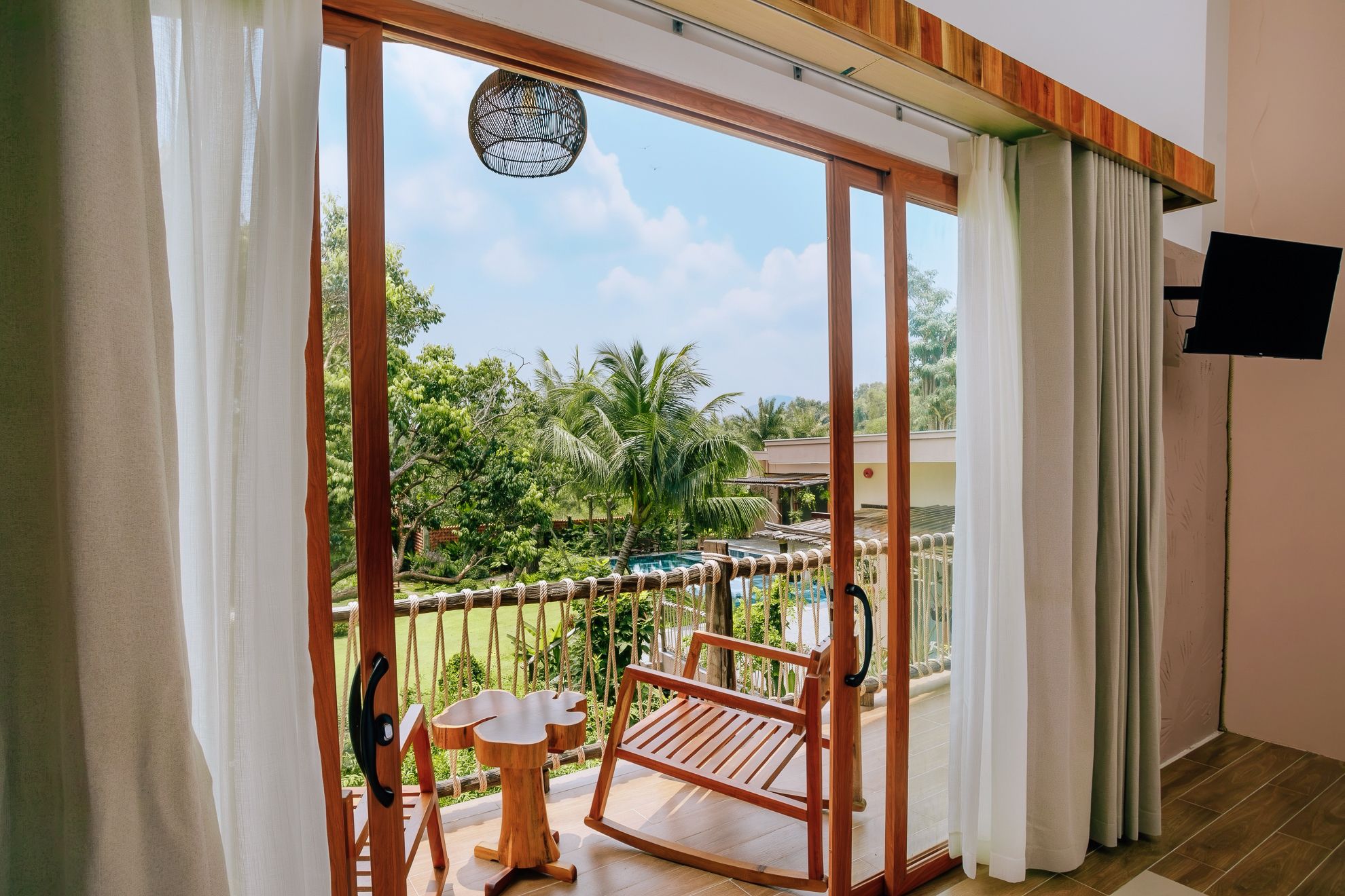 A room with a sliding glass door leading to a balcony with a wooden swing chair and a small table.