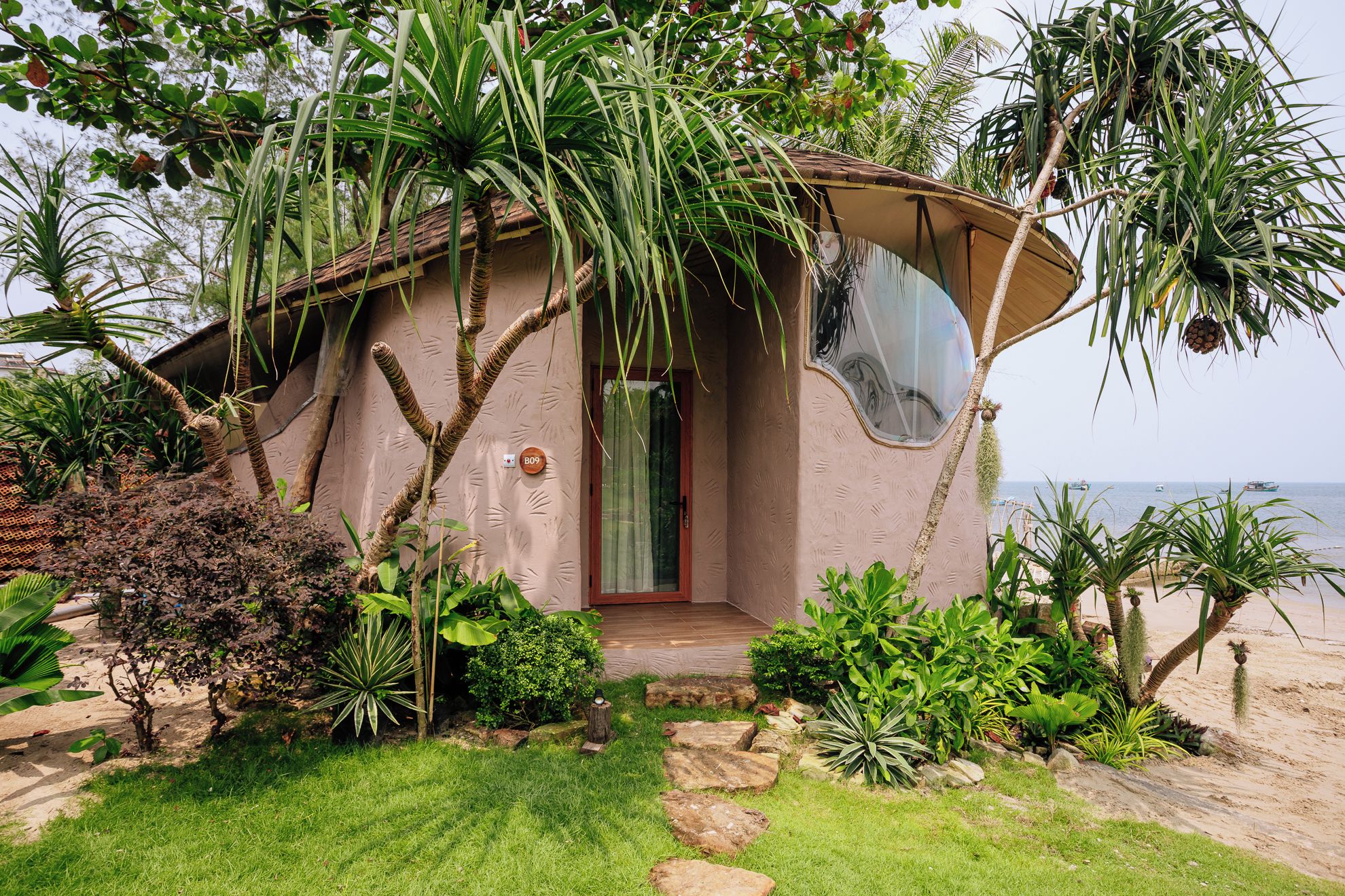 A beachfront house with a curved roof, a small porch, and a view of the sea.
