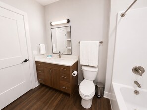 A bathroom with a toilet, sink, mirror, and a shower area. - Sleepover | Dashing Studio + Gym/Sauna + Omaha (Omaha)