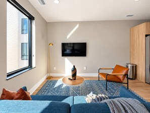 A modern living room with a sofa, a coffee table, a TV, and a floor lamp. - Sleepover | Dashing Studio + Gym/Sauna + Omaha (Omaha)