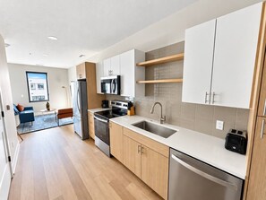 A modern kitchen with a dishwasher, oven, microwave, and a sink. - Sleepover | Dashing Studio + Gym/Sauna + Omaha (Omaha)