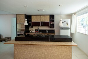Eine Küche mit einer zentralen Kochinsel, schwarzen Arbeitsplatten, Holzschränken, einem Kühlschrank und Pendelleuchten.