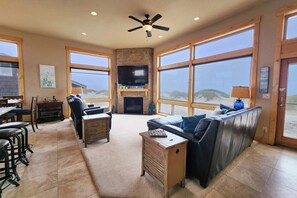 A spacious living room with a fireplace, large windows, and a ceiling fan. - Luxurious Home Sits Right on the Beach! Pet Friendly! (Waldport)