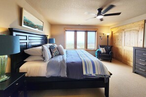 A bedroom with a bed, a nightstand, a dresser, a chair, a ceiling fan, and a window with a view. - Luxurious Home Sits Right on the Beach! Pet Friendly! (Waldport)