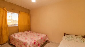 Un dormitorio con dos camas, una con cubrecama floral y la otra con un estampado de hojas verdes.