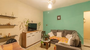 A living room with a sofa, a television on a wooden cabinet, and a ceiling fan. - House with BBQ in Vila Beira Rio - Ubatuba (Ubatuba)