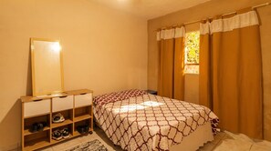 A bedroom with a bed, a bedside table, a mirror, and a window with curtains. - House with BBQ in Vila Beira Rio - Ubatuba (Ubatuba)