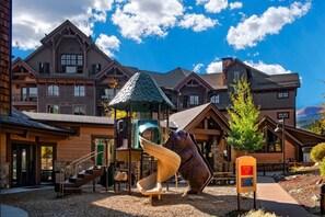 A lodge with a playground, including slides and climbing structures, in front of a building with a steep roof and multiple windows. - Grand Lodge Peak 7-Ski-In Ski-Out Breck Condo, Mtn Views, Resort Amenities, Sleeps 16 (Breckenridge)
