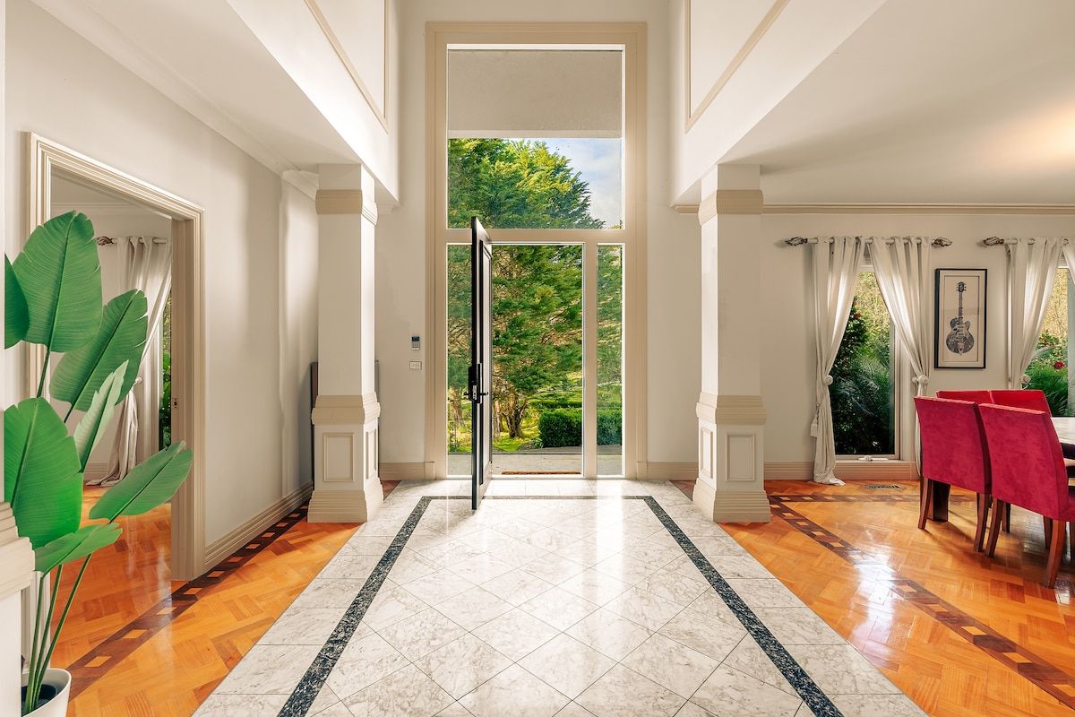 Un pasillo amplio con piso de madera, detalle de borde de mármol y vista a un jardín a través de un ventanal.