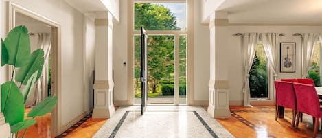 A spacious hallway with a wooden floor, a marble border, and a view of a garden through a glass door.
