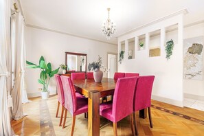 A dining room with a wooden table, six pink upholstered chairs, a chandelier, and decorative plants. - Warrandyte Bush Retreat  6BR with Private Pool (Warrandyte)