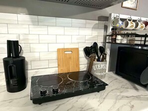 Cocina con tope de inducción negro, tabla de cortar de madera y un portalápices con la etiqueta 'UTENSIL'.