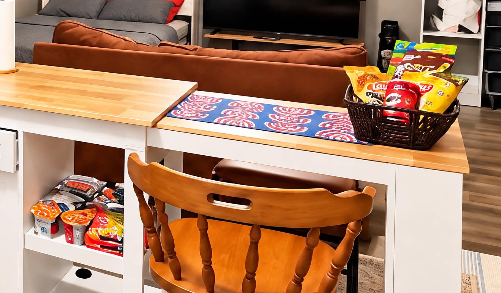 A kitchenette with a wooden chair, a table with a patterned placemat, and a basket of snacks.