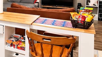 A kitchenette with a wooden chair, a table with a patterned placemat, and a basket of snacks.