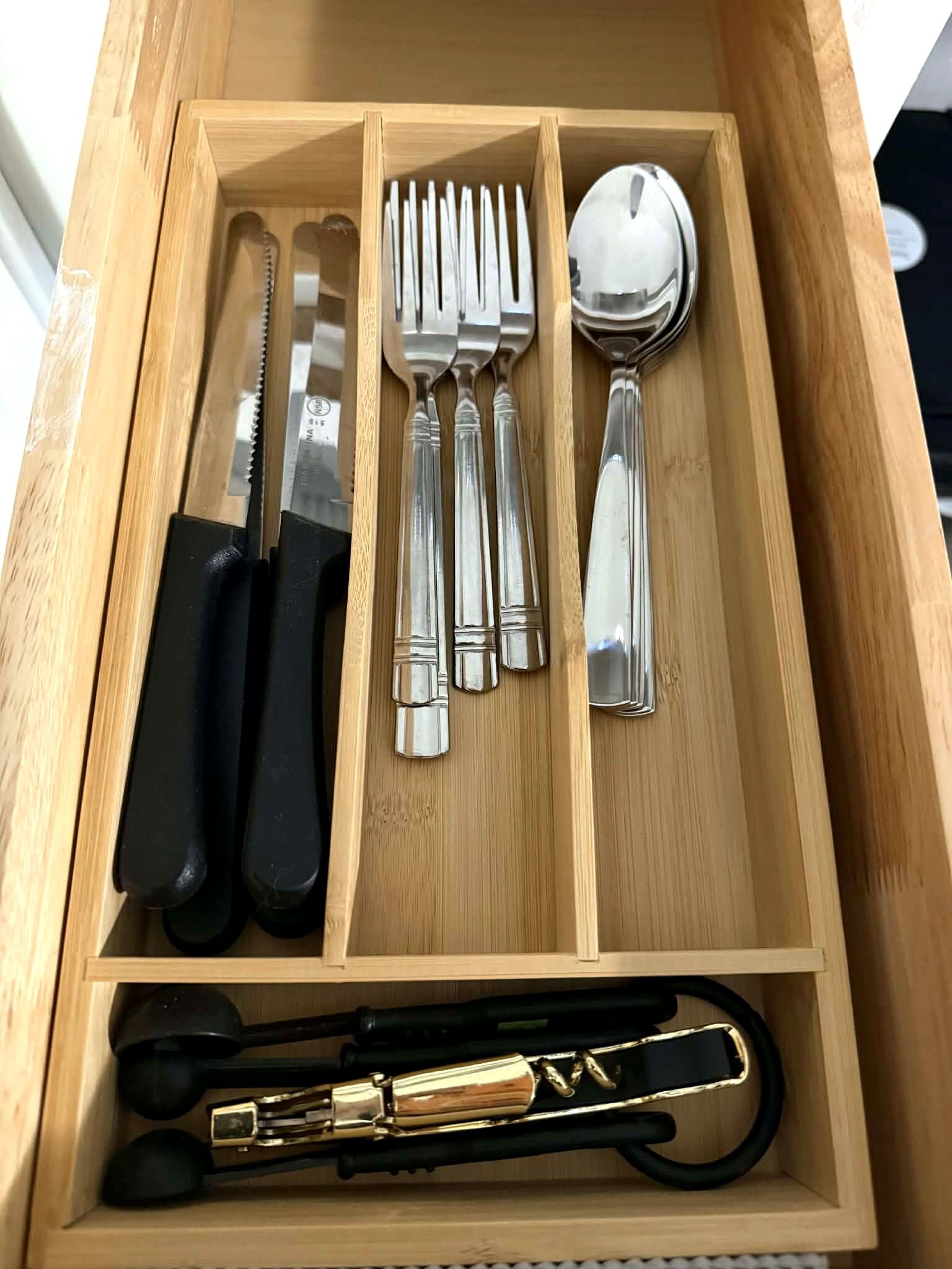 A wooden drawer with a set of silverware including a knife, forks, spoons, and a pair of chopsticks.