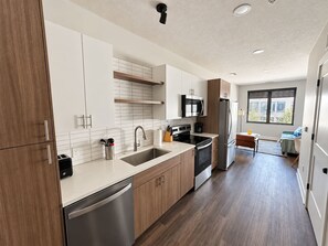 A modern kitchen with stainless steel appliances, wooden cabinets, and a large window providing natural light. - Sleepover | Peaceful Studio + Gym/Sauna - Omaha (Omaha)