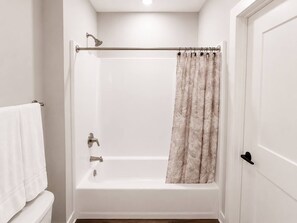 A bathroom with a white bathtub, a showerhead, and a curtain. - Sleepover | Peaceful Studio + Gym/Sauna - Omaha (Omaha)