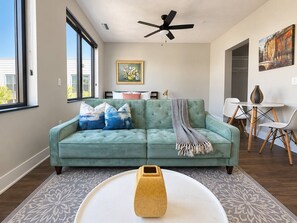 A living room with a teal sofa, a coffee table, and a painting on the wall. - Sleepover | Peaceful Studio + Gym/Sauna - Omaha (Omaha)