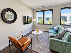 A modern living room with a sofa, a chair, a coffee table, and a TV mounted on the wall. - Sleepover | Peaceful Studio + Gym/Sauna - Omaha (Omaha)