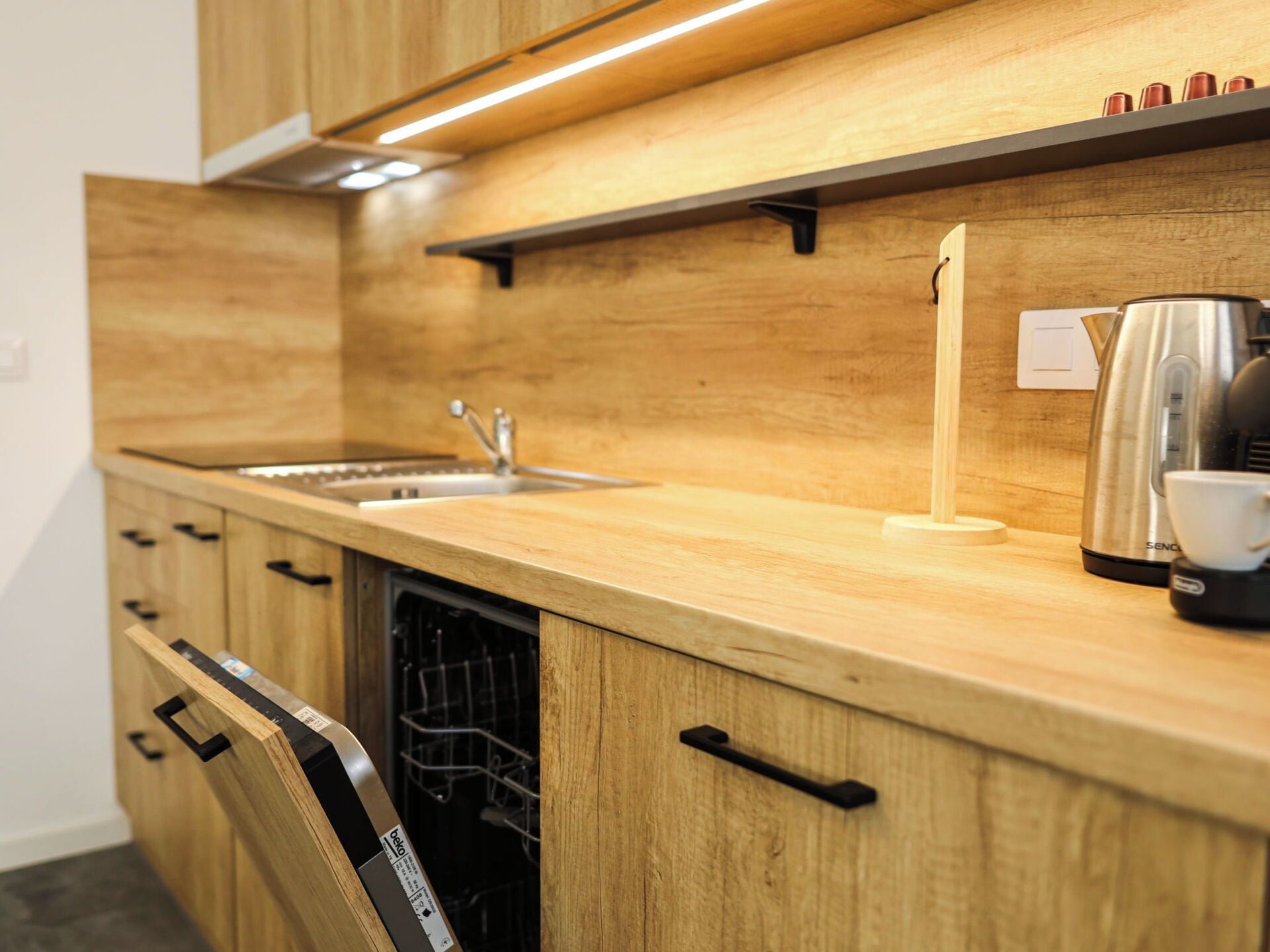 Una cocina con gabinetes de madera, un lavamanos de acero inoxidable, un lavavajillas y una cafetera.