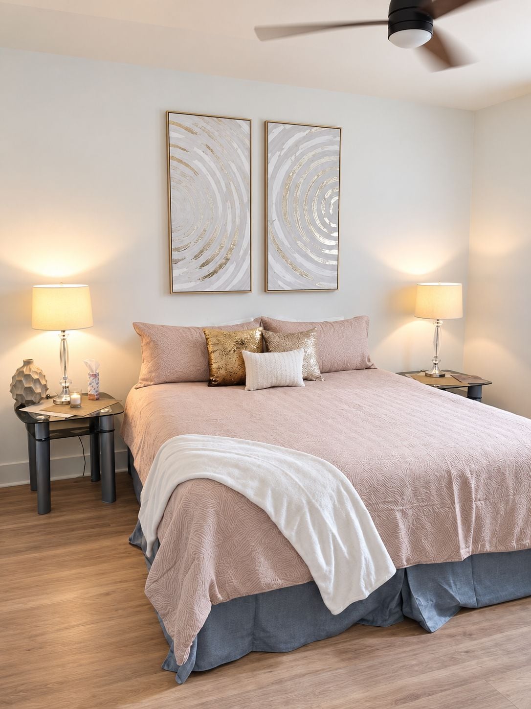 Une chambre à coucher avec un lit, deux tables de chevet, des lampes et des œuvres d’art abstraites accrochées au mur.